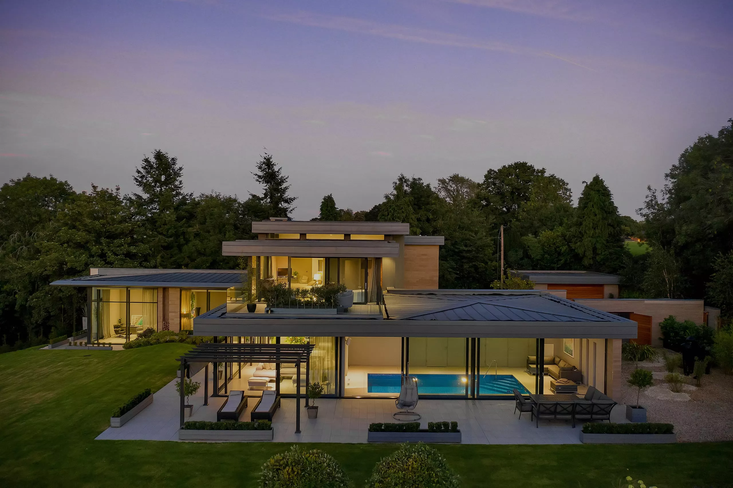 Modern smart home lit at dusk with pool and automated lighting