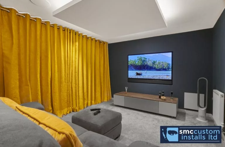 Media room with wall-mounted TV, full-height mustard curtains and recessed coffered ceiling lighting