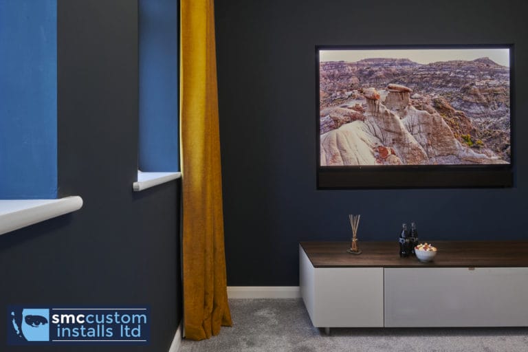 Wall-mounted TV on navy wall above low media unit with window blind, snug