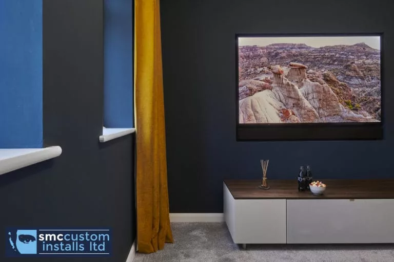 Wall-mounted TV on navy wall above low media unit with window blind, snug