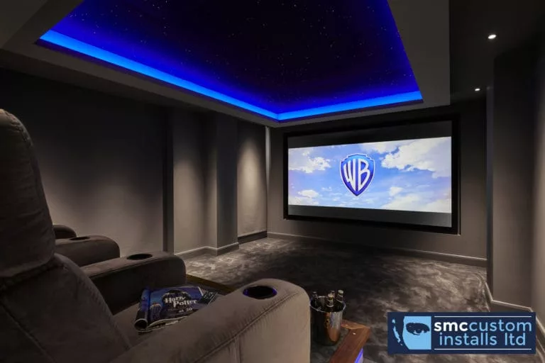 Cinema recliners facing projection screen beneath star ceiling with blue cove lighting