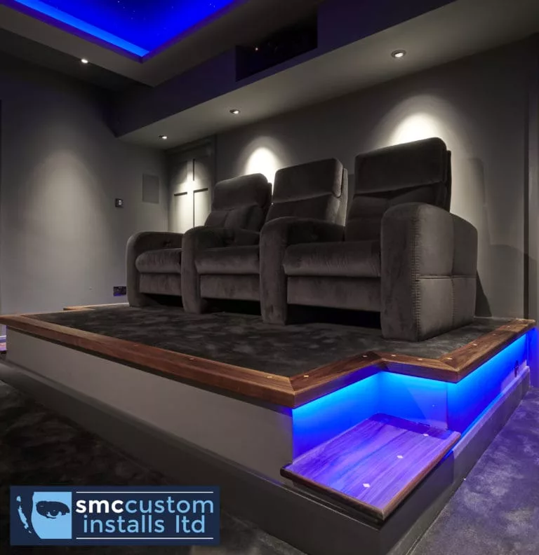 Velvet cinema recliners on walnut-edged platform with blue LED step lighting, dedicated cinema room