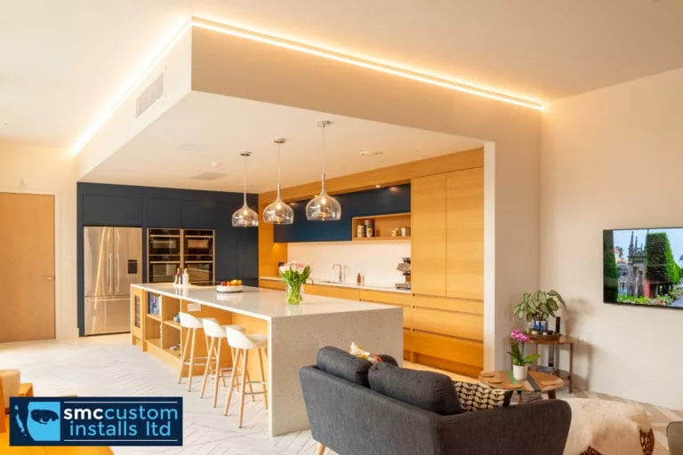 Open-plan kitchen with recessed LED strip lighting, island pendants and wall-mounted TV