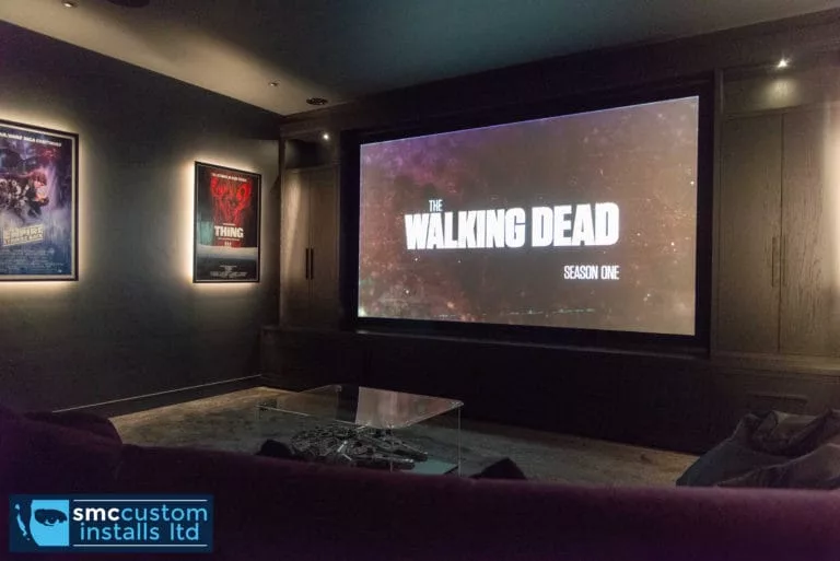Projection screen showing film titles beside backlit posters in dedicated home cinema room