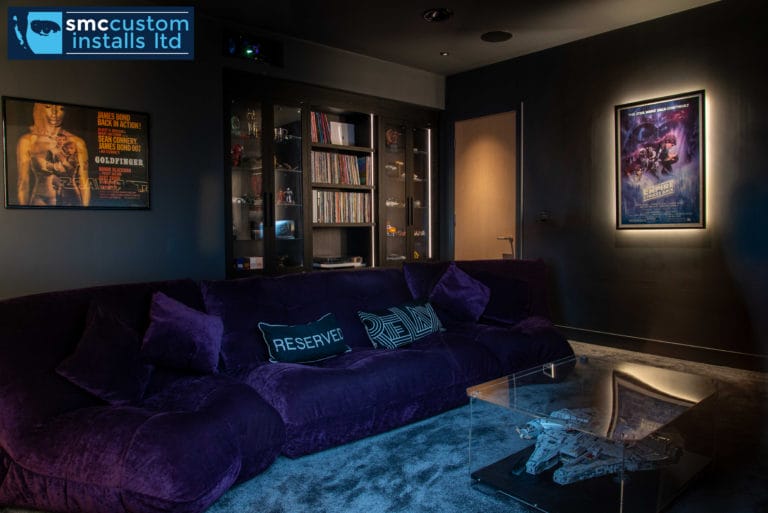 Cinema snug with purple velvet sofa, backlit film posters and glazed media cabinet