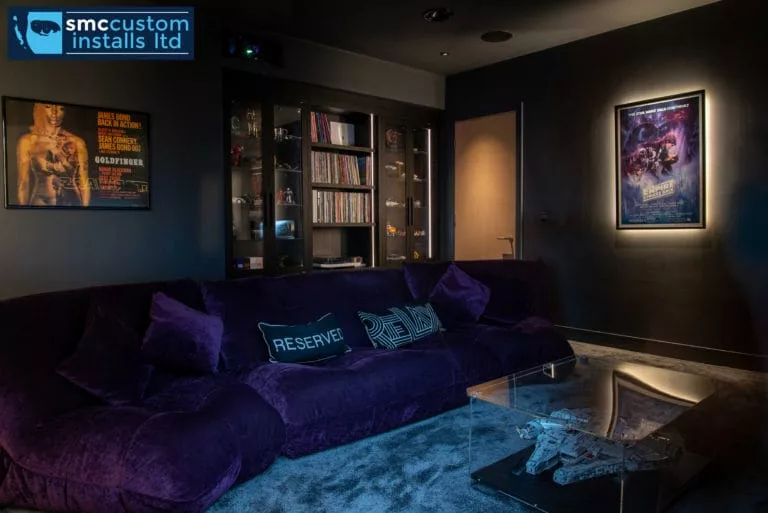 Cinema snug with purple velvet sofa, backlit film posters and glazed media cabinet