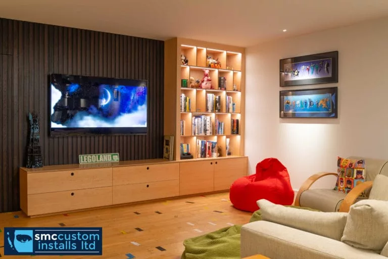 Living room media wall with TV on slatted panelling and illuminated oak bookcase