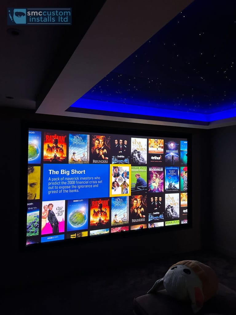 Cinema projection screen showing film menu beneath a starlight ceiling with blue coving