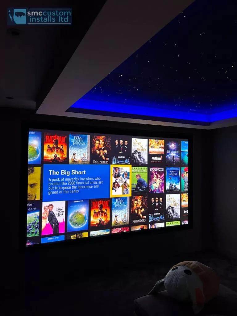 Cinema projection screen showing film menu beneath a starlight ceiling with blue coving
