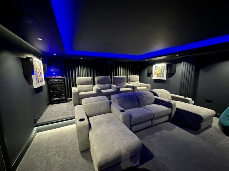 Rows of grey velvet cinema recliners under blue LED cove ceiling, dedicated home cinema