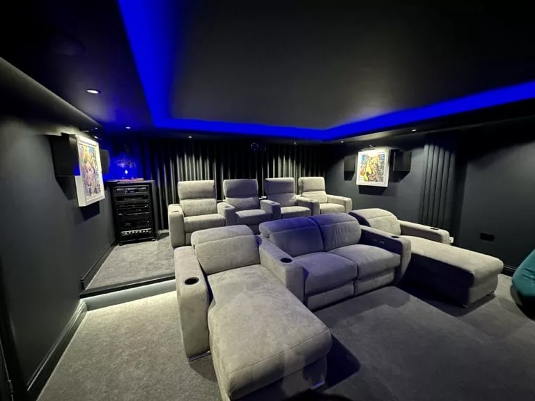 Rows of grey velvet cinema recliners under blue LED cove ceiling, dedicated home cinema