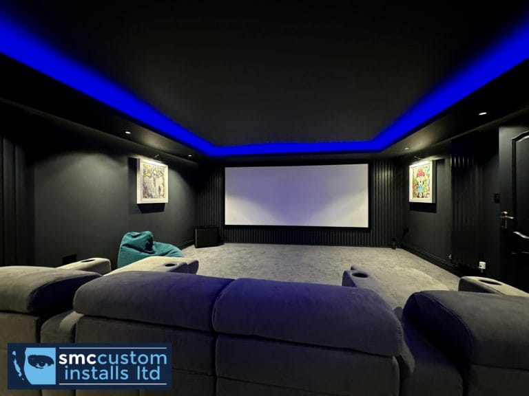 Dedicated home cinema room with projector screen, blue LED coving and grey sofa seating