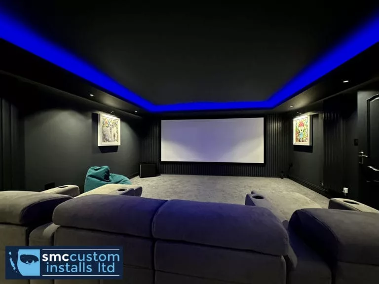 Dedicated home cinema room with projector screen, blue LED coving and grey sofa seating