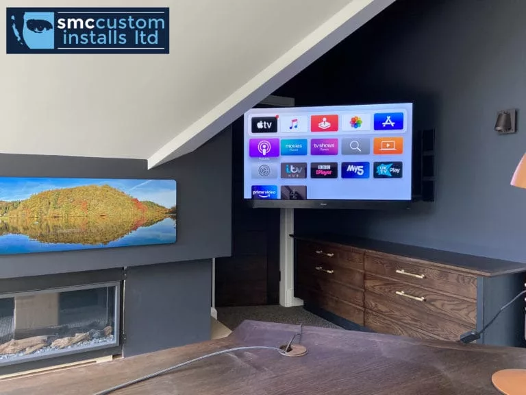 Corner wall-mounted TV showing Apple TV apps above fitted cabinetry in a loft room