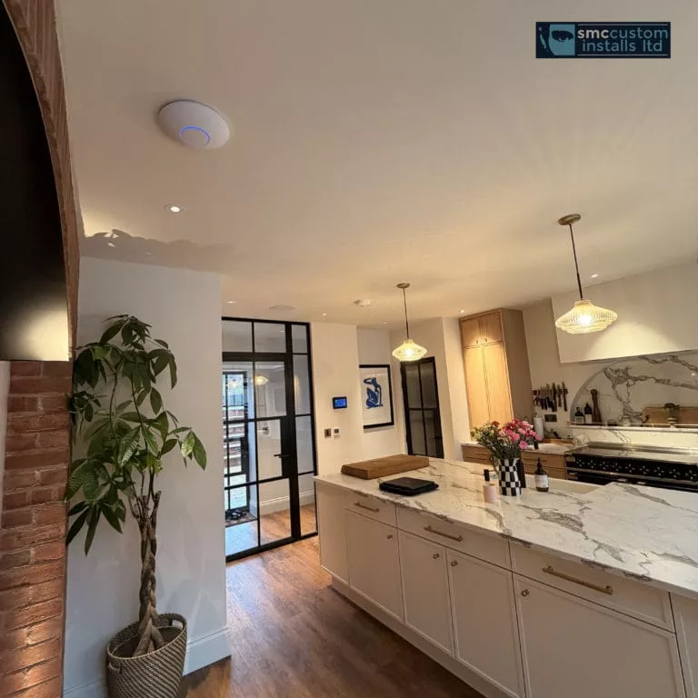 Kitchen with marble island, in-ceiling speaker and wall-mounted keypad beside Crittall doors