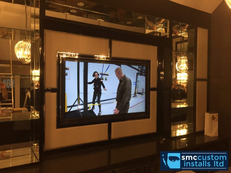 Wall-mounted TV framed within a mirrored black media wall with feature lighting