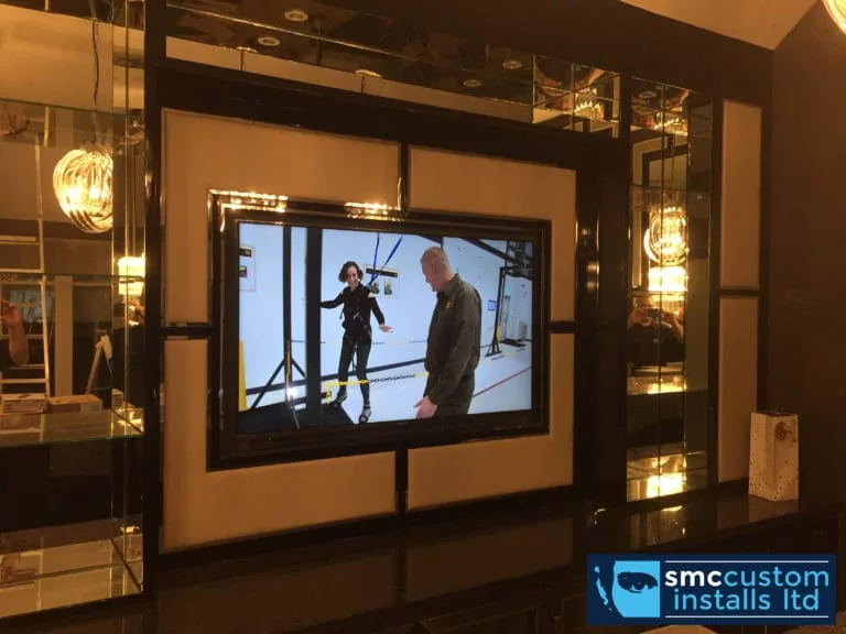 Wall-mounted TV framed within a mirrored black media wall with feature lighting