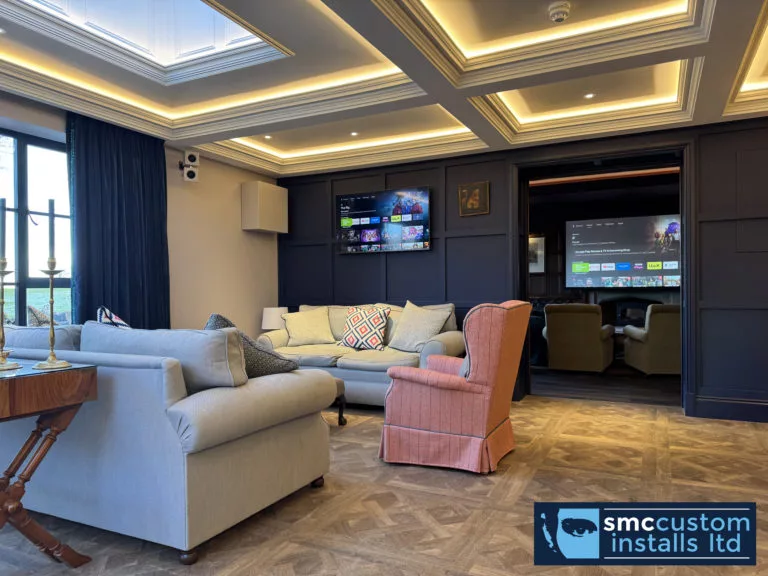 Wall-mounted TVs and speakers in a blue-panelled bar lounge with LED coffered ceiling