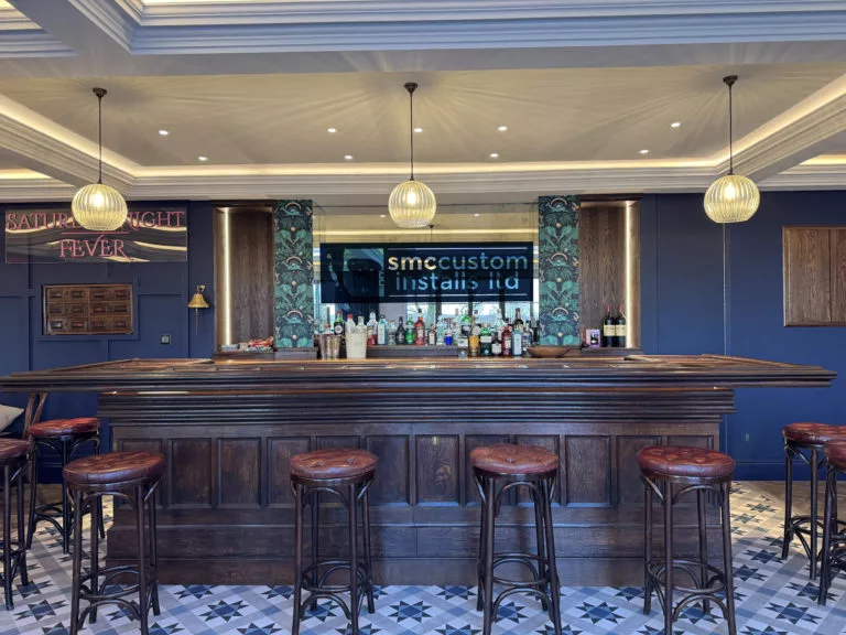 Bespoke home bar with stools, pendant lights and a TV mounted behind the counter