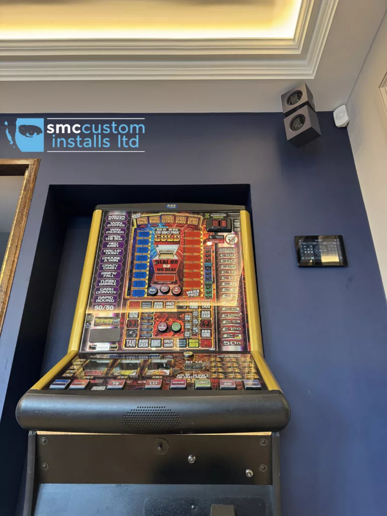 Wall-mounted speaker and touch panel above a fruit machine in the games room