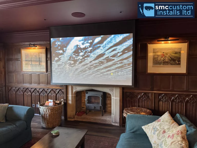 Projector screen lowered over a stone fireplace and stove in an oak-panelled lounge