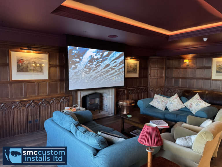 Drop-down projector screen above a stone fireplace in a wood-panelled lounge cinema