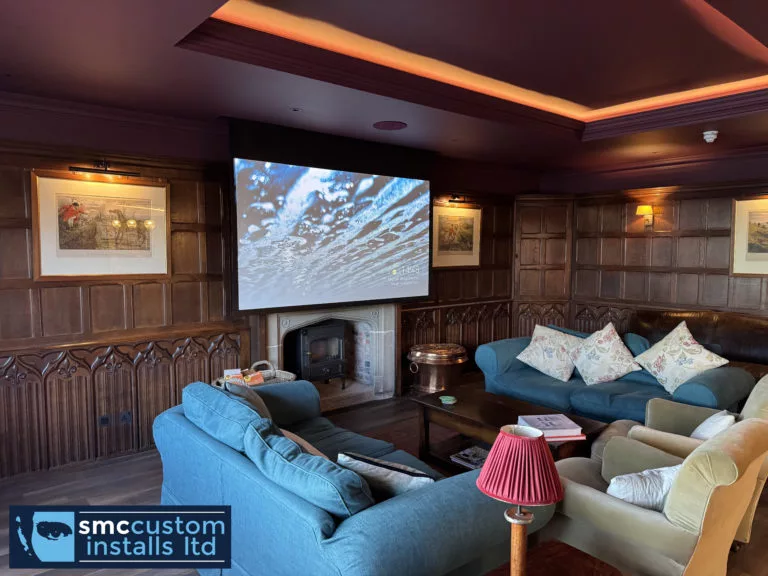 Drop-down projector screen above a stone fireplace in a wood-panelled lounge cinema