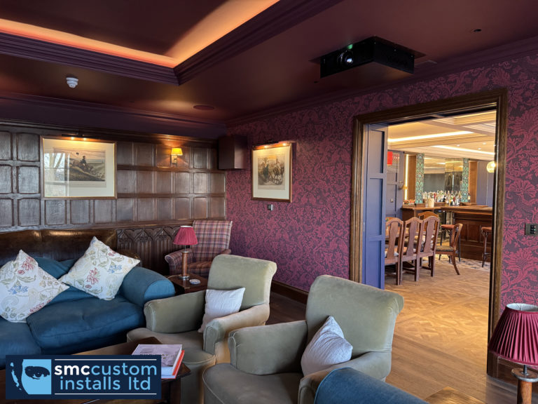 Ceiling-mounted projector in a panelled lounge cinema, looking through to the bar area