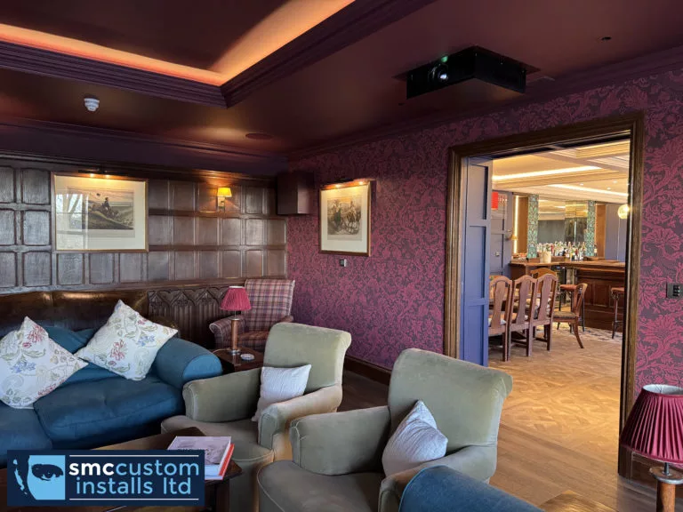 Ceiling-mounted projector in a panelled lounge cinema, looking through to the bar area