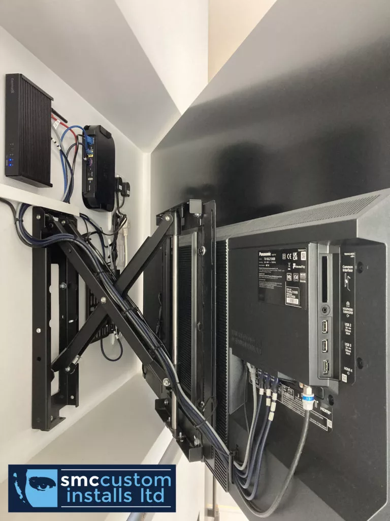 Articulated TV wall bracket with tidy cable management and wall-mounted AV equipment behind the screen