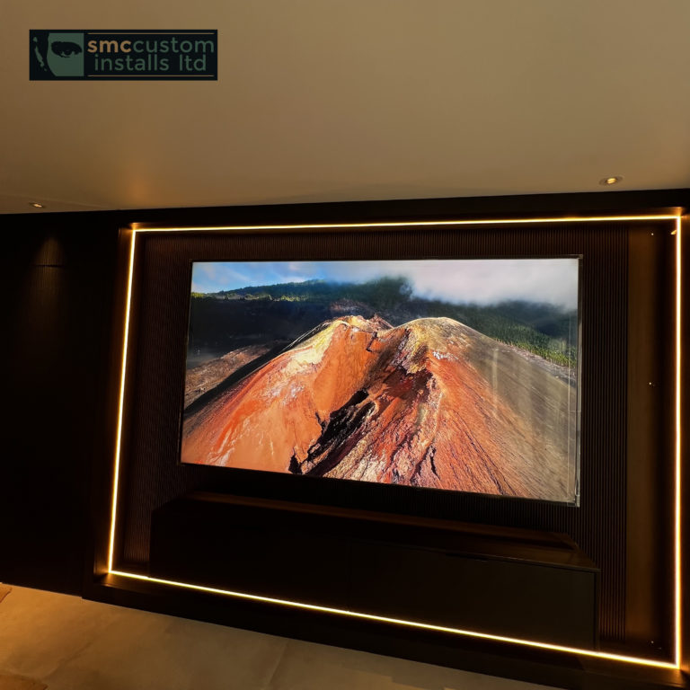 Wall-mounted TV on a dark media wall framed by warm LED strip lighting