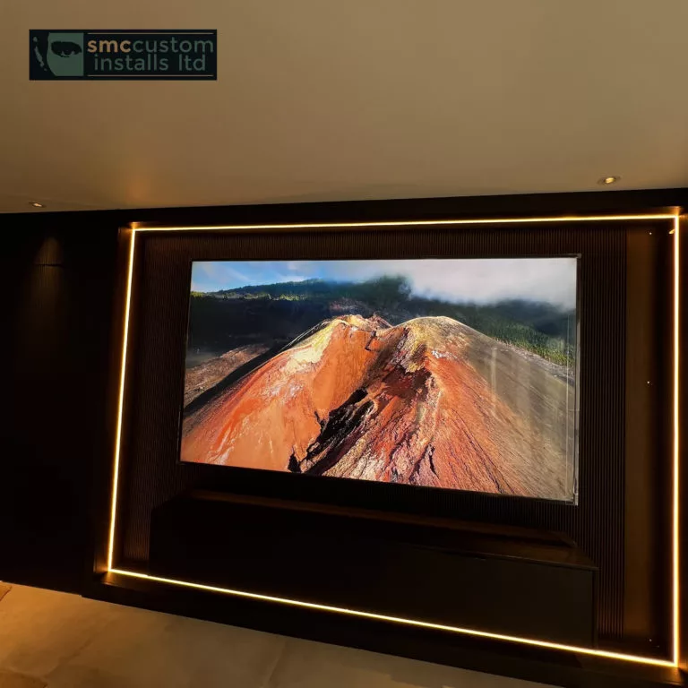 Wall-mounted TV on a dark media wall framed by warm LED strip lighting