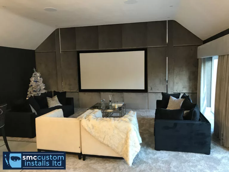 Cinema room with projection screen on fabric-panelled wall and dark sofa seating