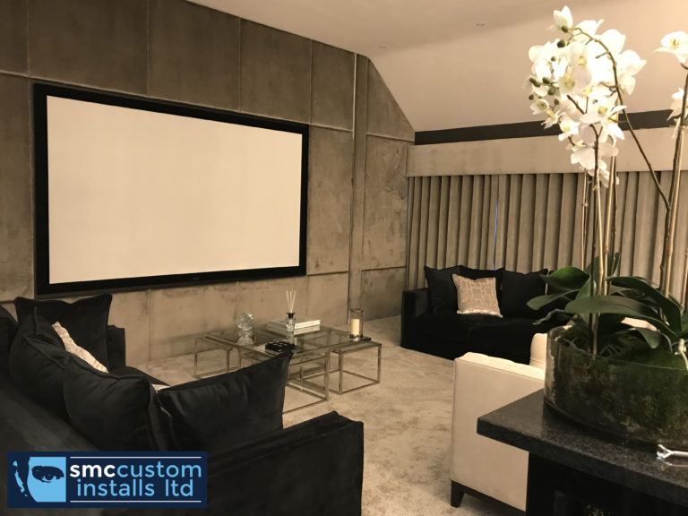 Cinema room with projection screen, suede wall panels and dark sofas around glass tables