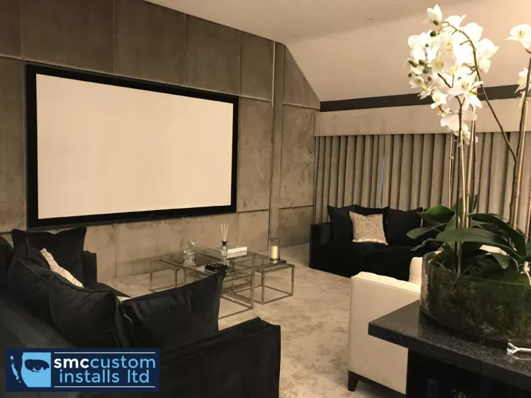 Cinema room with projection screen, suede wall panels and dark sofas around glass tables