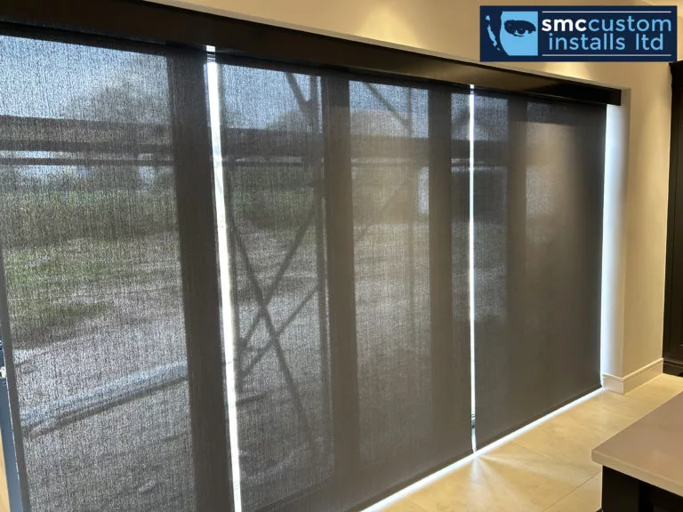 Motorised sunscreen roller blinds lowered across a wide run of glazed doors