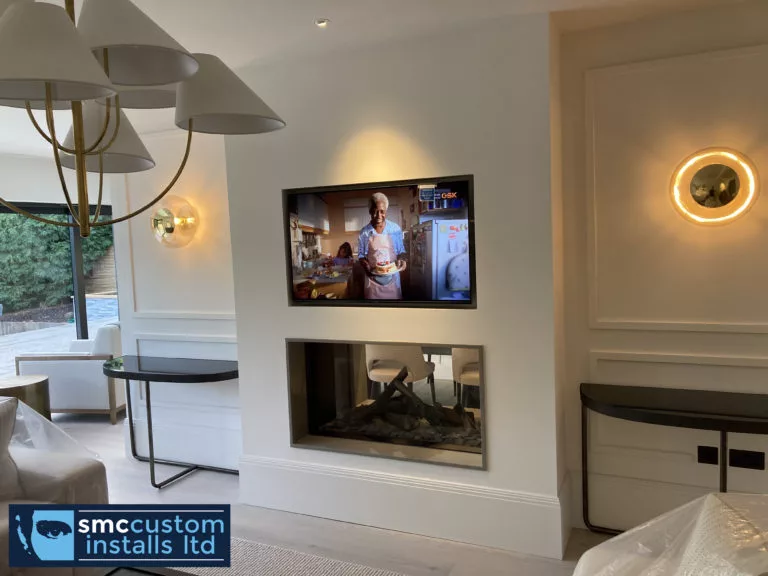 Wall-mounted TV above an inset fireplace with panelled walls and brass sconces