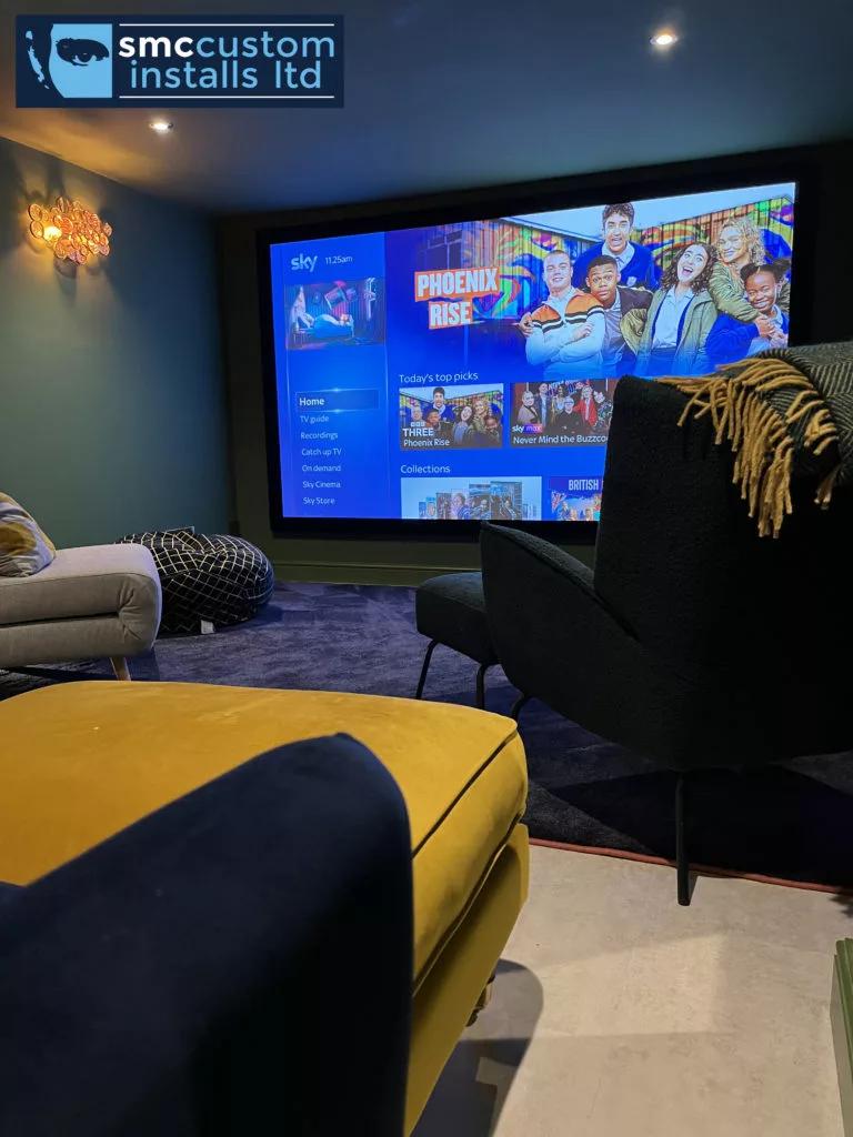 Home cinema room with projection screen, teal walls and velvet armchair seating