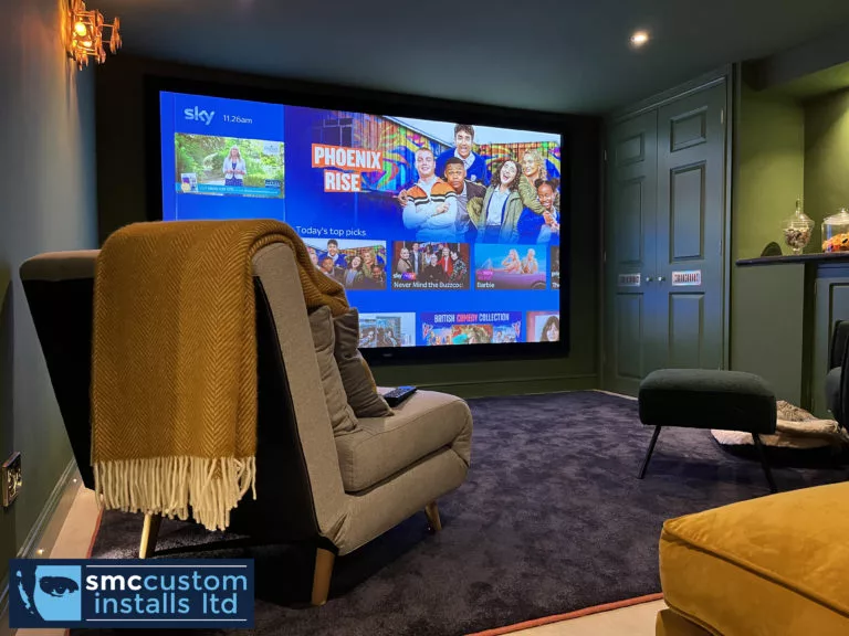 Cinema room armchairs facing a large projection screen against green panelled walls