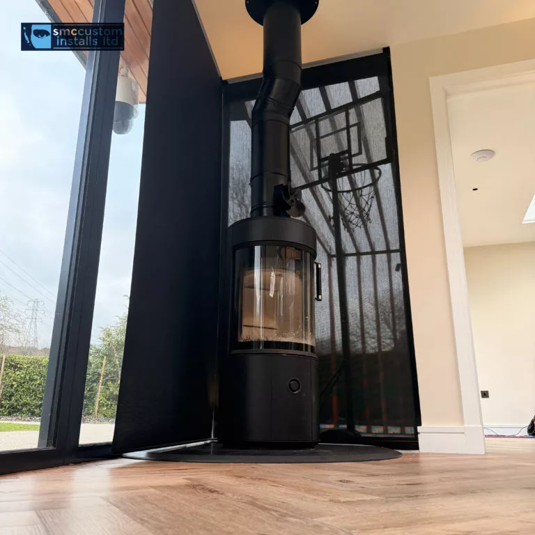 Black wood-burning stove in a glazed corner with in-ceiling speaker above