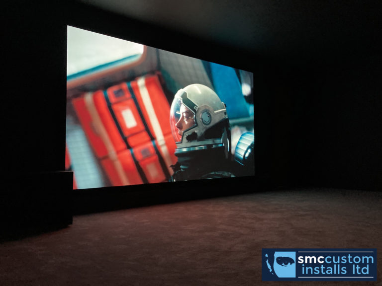 Dedicated home cinema room with large projection screen showing a film in darkness