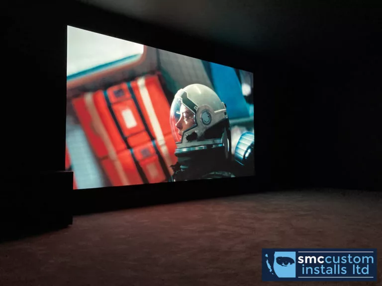 Dedicated home cinema room with large projection screen showing a film in darkness