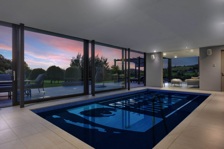 Indoor swimming pool with floor-to-ceiling glazing and countryside views at dusk