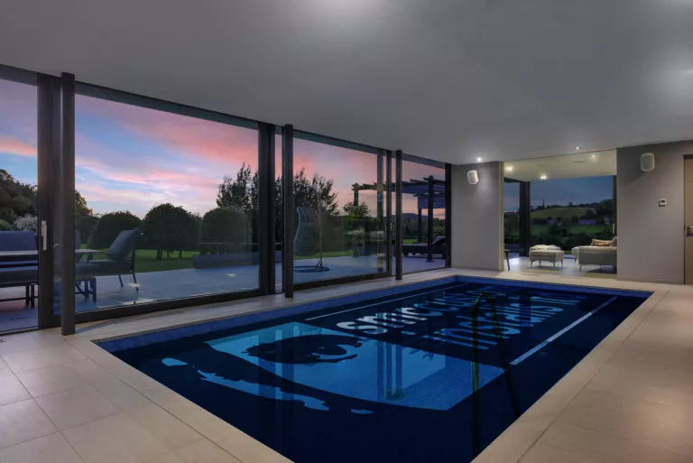 Indoor swimming pool with floor-to-ceiling glazing and countryside views at dusk