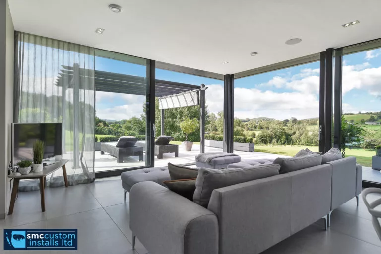 Living room with corner sofa, sheer curtains and glazed doors opening to patio seating