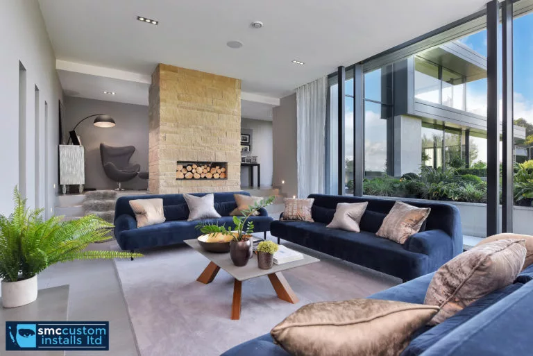 Open-plan living room with navy sofas, stone fireplace and full-height corner glazing
