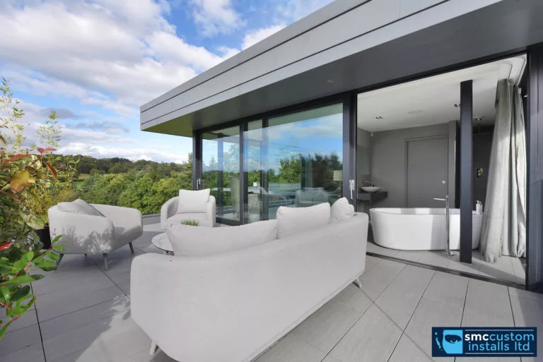 Roof terrace with white sofas beside glazed sliding doors to a bathroom suite